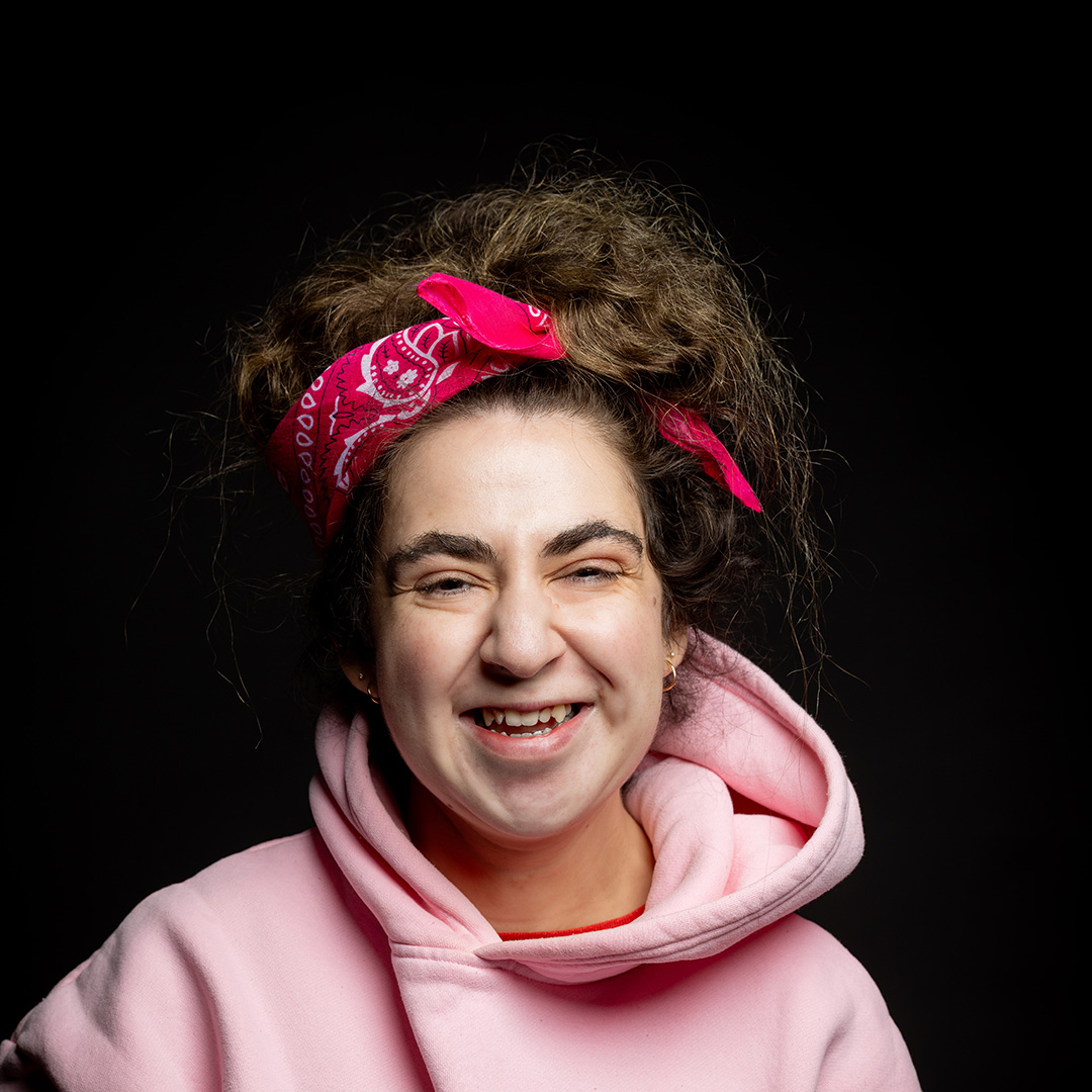 Mia - Harrow College Foundation Learning student - wearing a pink hoodie and a pink scarf in her hair which is pulled up on top of her head. She has a big smile.