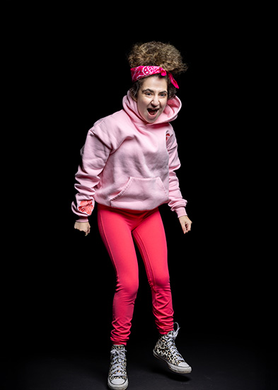 Mia - Harrow College Foundation Learning student - wearing a pink hoodie, a pink scarf in her hair with pink leggings. It looks like she is about to jump up and her mouth is open.