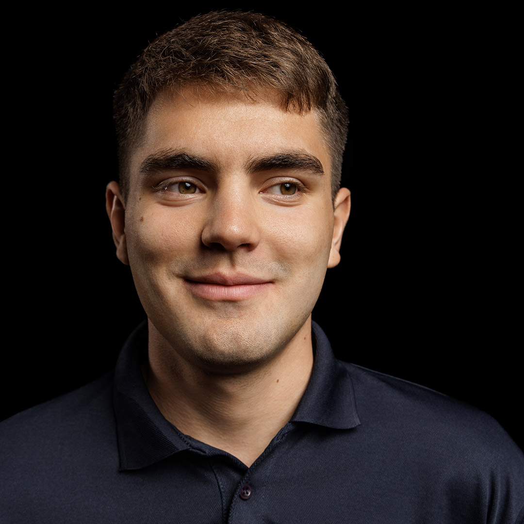 Cristian is looking off to the side and smiling. He is wearing a navy polo shirt. 