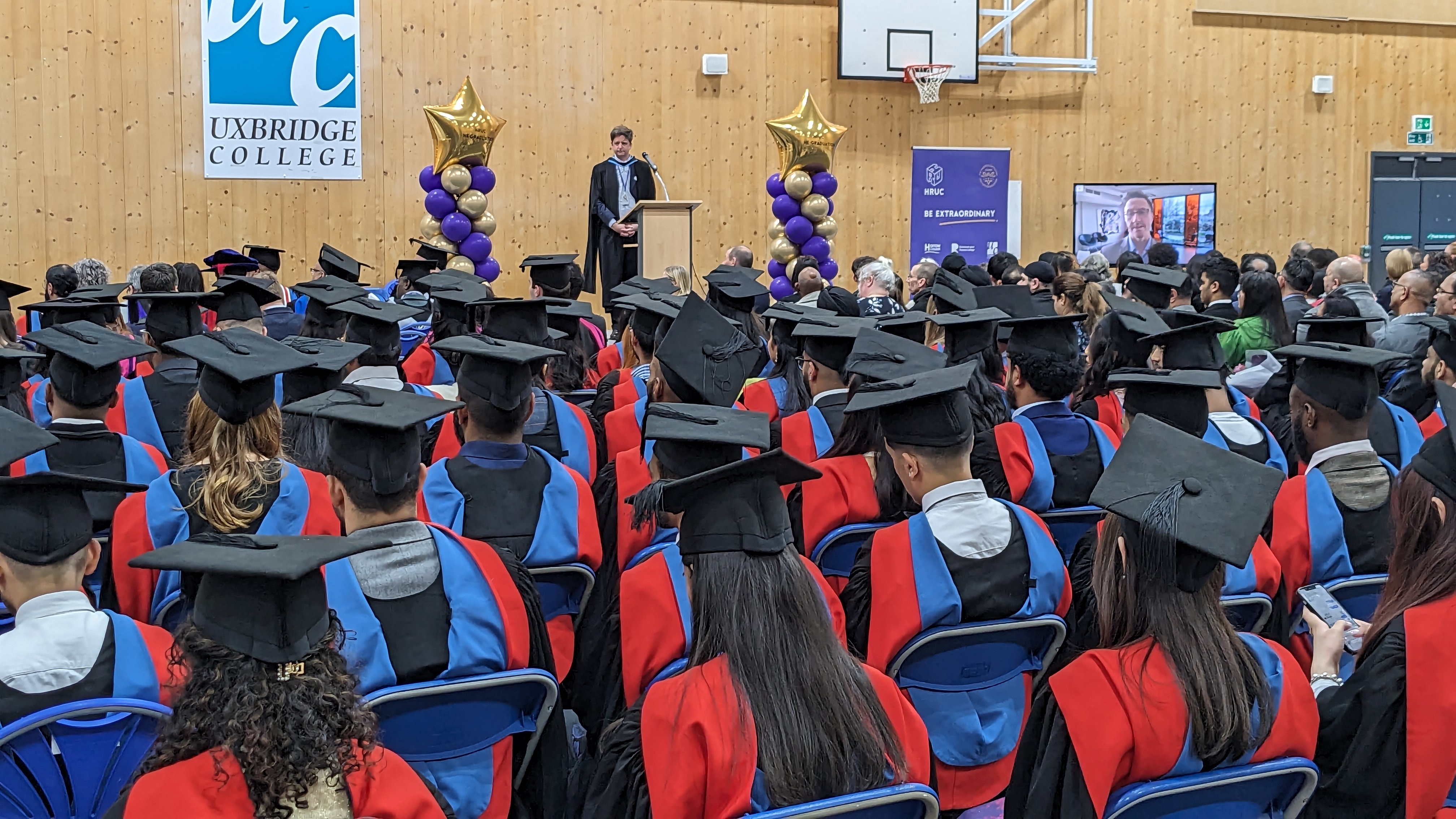 Shot of Dylan, Principle of Uxbridge, giving a speech to graduates and their families.