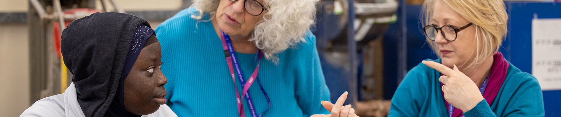 Harrow Weald SEN student working with two female staff members in a workshop on an art project. The staff members are both wearing blue tops and glasses.