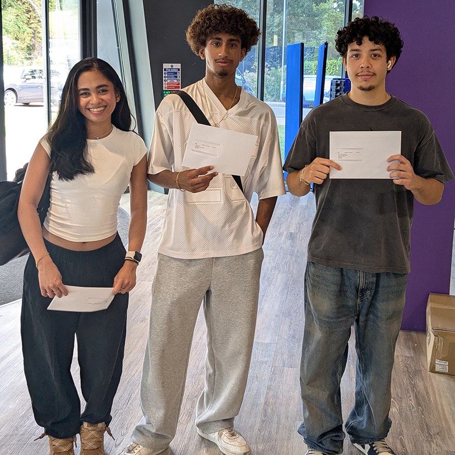 Three Harrow College students holding up their results letters. Standing in reception at Harrow on the Hill College.
