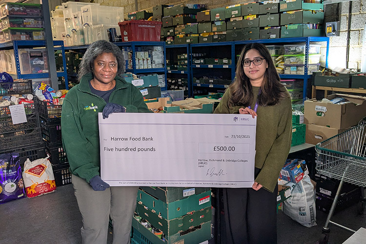 Yashvi Prajapati (Employee Experience Administrator)  presented a ceremonial cheque signed by HRUC CEO, Keith Smith, to Chonde Nkowani, Manager at Harrow Food Bank. They are standing in front of the shelves of food donations.