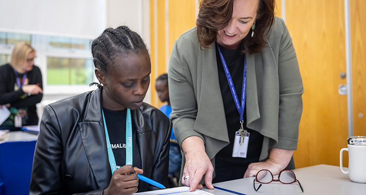 A Harrow teacher instructing a Harrow Science student. Both are looking down at paperwork.