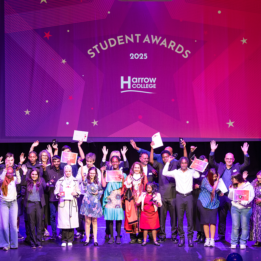2025 Harrow College Student Awards evening - all award winners on stage, smiling and holding their hands and awards in the air. Standing in front of a big digital screen of a red awards sign.