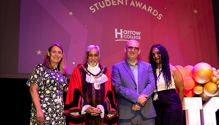 Jo Swindells, Principal of Harrow College, standing on stage with The Worshipful Mayor of the London Borough of Hillingdon, Councillor Yogesh Teli, with Sultan Soukani and Kelly Ocloo - Assistant Principals at Harrow College - at the Harrow College 2026 Student Awards ceremony. Thre is a red screen beind them with the words: Student Awards and Harrow College.