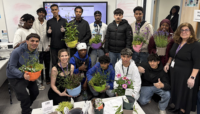 Harrow College ESOL students with teaching staff gathered together in the classroom holding plants for the community garden project.