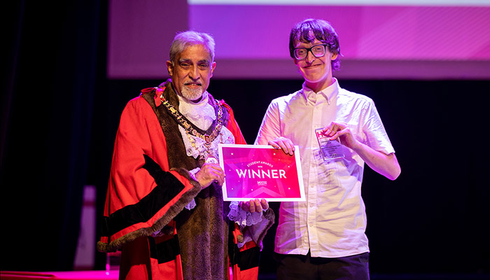 Leo Gilby - other winner of the Greatest Contribution to College Life award standing with The Worshipful Mayor of the London Borough of Hillingdon, Councillor Yogesh Teli. Leo is holding his award and they are both holding his certificate. The mayor is in his ceremonial robes and there is a screen behind them.