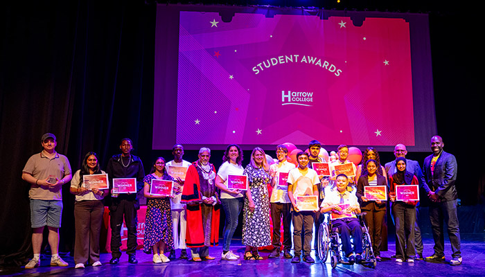 Group photo of all the winners from the Harrow College Student Awards ceremony 2026. They are standing on stage, holding their 'Winner' certificates with a big screen behind them that says Student Awards - Harrow College.