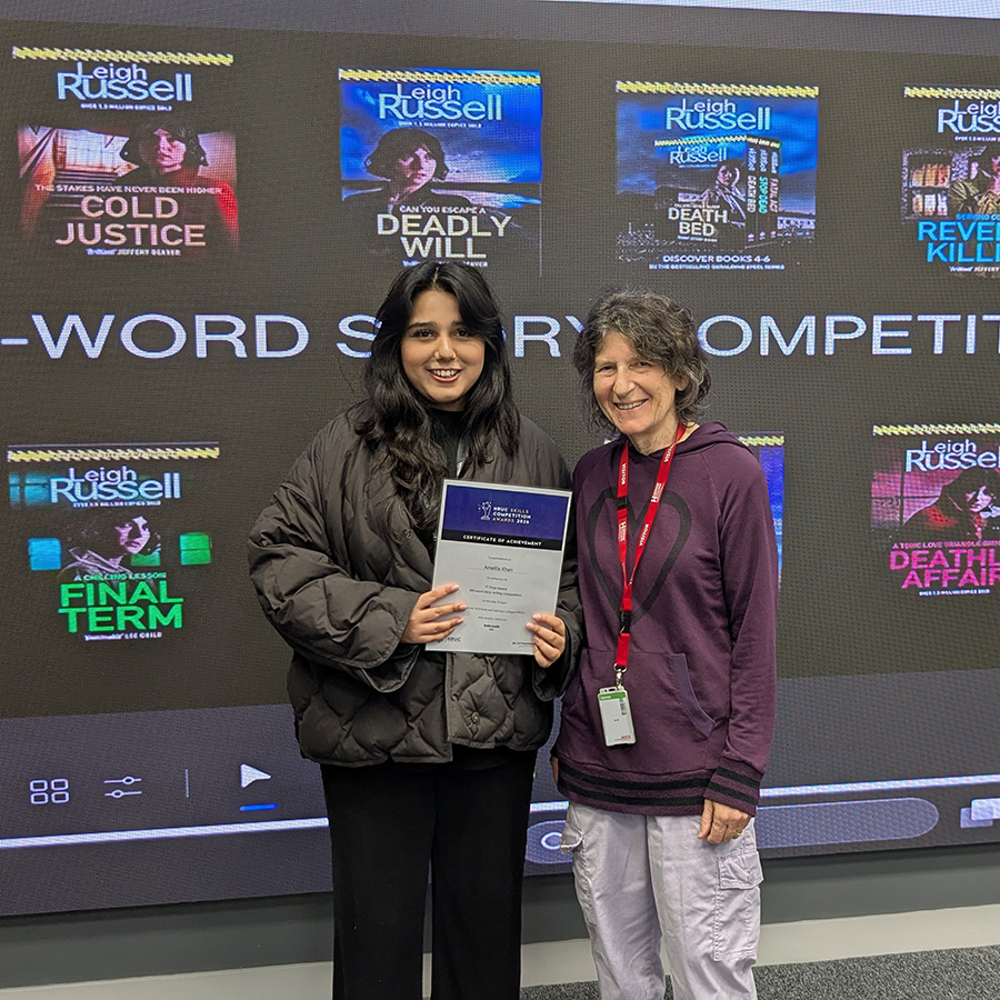 Ameila Khan - 2nd prize competition winner in the Young Writers Stranger Sagas competition standing with Leigh Russell and holding her certifcate. They are standing in front of a screen with Leigh Russell's books displayed on it. 