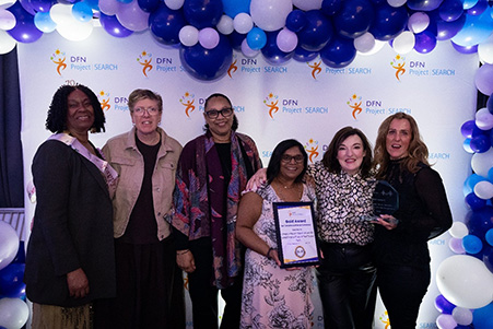 6 female colleagues from Harrow College, smiling at the camera in front of a 'dfn project search' graphic with blue and white balloons above and to the right side.
