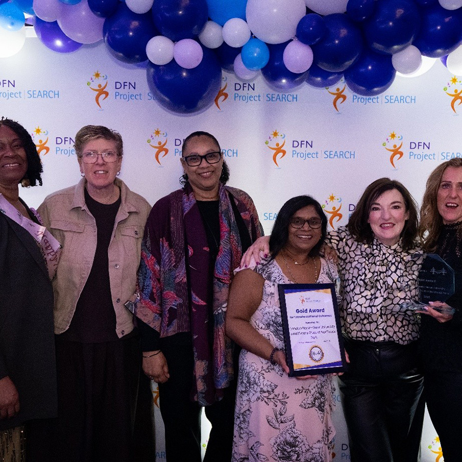 6 female colleagues from Harrow College, smiling at the camera in front of a 'dfn project search' graphic with blue and white balloons above and to the right side.
